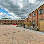 Brick homes with paved driveway and cloudy sky.