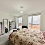 Bright bedroom with floral bedspread and large window.