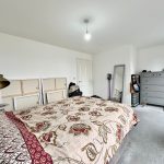 Spacious bedroom with patterned bedspread and grey dresser.