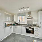 Modern white kitchen with sleek appliances and lighting.