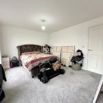Spacious bedroom with bed, paintings, and workout equipment.