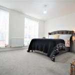 Modern bedroom with grey bed and large windows.