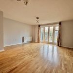 Spacious empty room with wooden flooring and doors.
