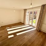 Sunlit room with wooden floor and garden view.