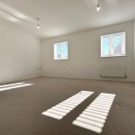 Bright empty room with windows and neutral carpet.