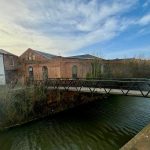 Brick warehouse by a canal and footbridge.