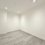 Empty white room with wooden flooring and spotlights.