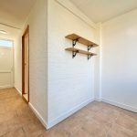 White brick corridor with wooden shelves and door.