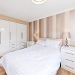 Modern bedroom with white furniture and striped wallpaper.