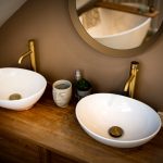 Modern bathroom sinks with gold taps and mirror.