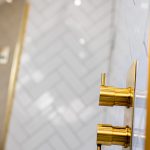 Gold shower knobs with herringbone tile background.