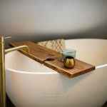 Modern bathtub with wooden tray and gold tap.