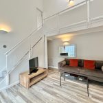 Modern living room with TV, sofa and staircase.