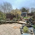 Peaceful garden with patio, chairs, and pond view.