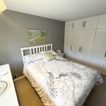 Cosy bedroom with floral bedding and white wardrobes.