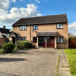 Semi-detached brick house with driveway in sunny weather.