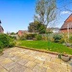 Sunny garden with patio and greenery.