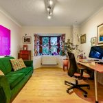 Bright home office with green sofa, desk, and computer.