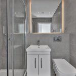 Modern grey bathroom with shower and illuminated mirror.