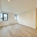 Spacious modern room with wooden flooring and windows.