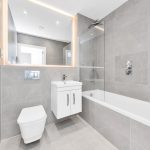 Modern grey tiled bathroom with bathtub and mirror.
