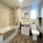 Modern bathroom with white fixtures and wooden flooring.