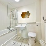 Modern bathroom with white tiles and hexagonal mirror.