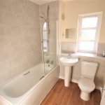 Modern bathroom with bathtub and wooden flooring.