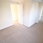 Empty carpeted room with open door and mirror.