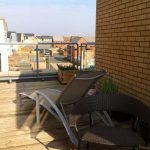 Sunny modern balcony with deck chairs and potted plants.