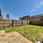 Sunny fenced garden with grass and patio area.