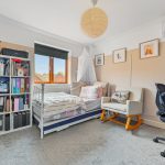Cosy bedroom with bed, chair, desk, and shelves.
