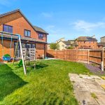 Back garden with swing set and red brick house.