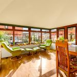 Bright conservatory with green chairs and dining table.