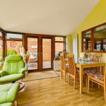 Bright conservatory with green chair and dining area.