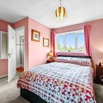 Cosy pink bedroom with patterned duvet and window view.