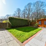 Sunny garden with wooden shed and patio.