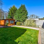 Sunny garden with wooden shed and patio area.