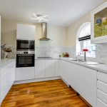 Modern kitchen with white cabinets and wooden flooring.