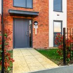 Entrance to modern building with brick facade and shrubs.
