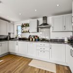 Modern white kitchen with wooden flooring and plants.