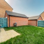 Back garden with grass and patio in housing estate.