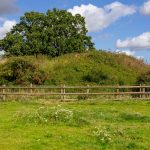 Green field with hill and wooden fence.