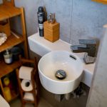 Modern small bathroom with sink and wooden shelf.