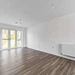Empty room with wooden flooring and large windows.