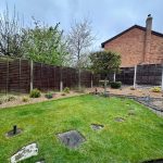 Garden with lawn, plants, fence, and house in background.