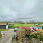 Countryside view with parked cars and cloudy sky.