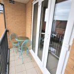 Balcony with glass table, chairs, view of street.