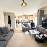 Modern living room with kitchen and baby items.