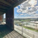 Balcony view with fields and building under blue sky.